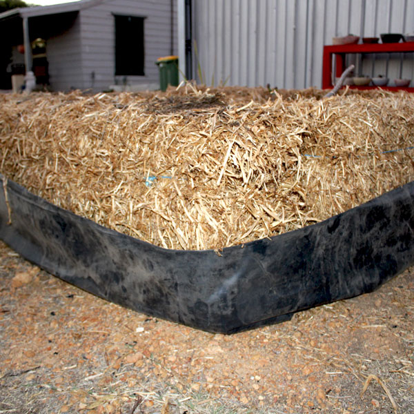 a bale of hay wrapped in black plastic, stage one of a haybale garden
