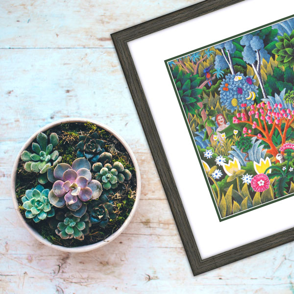 the framed jungle print on a weathered white floor next to some sculptural succulents 
