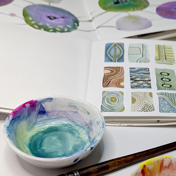 a sketchbook with a modern watercolour pattern painted in it with a pallette and bowl