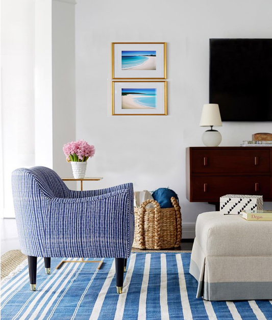 Two small framed prints of Mandys beach scenes on the wall of a blue striped themed loungeroom